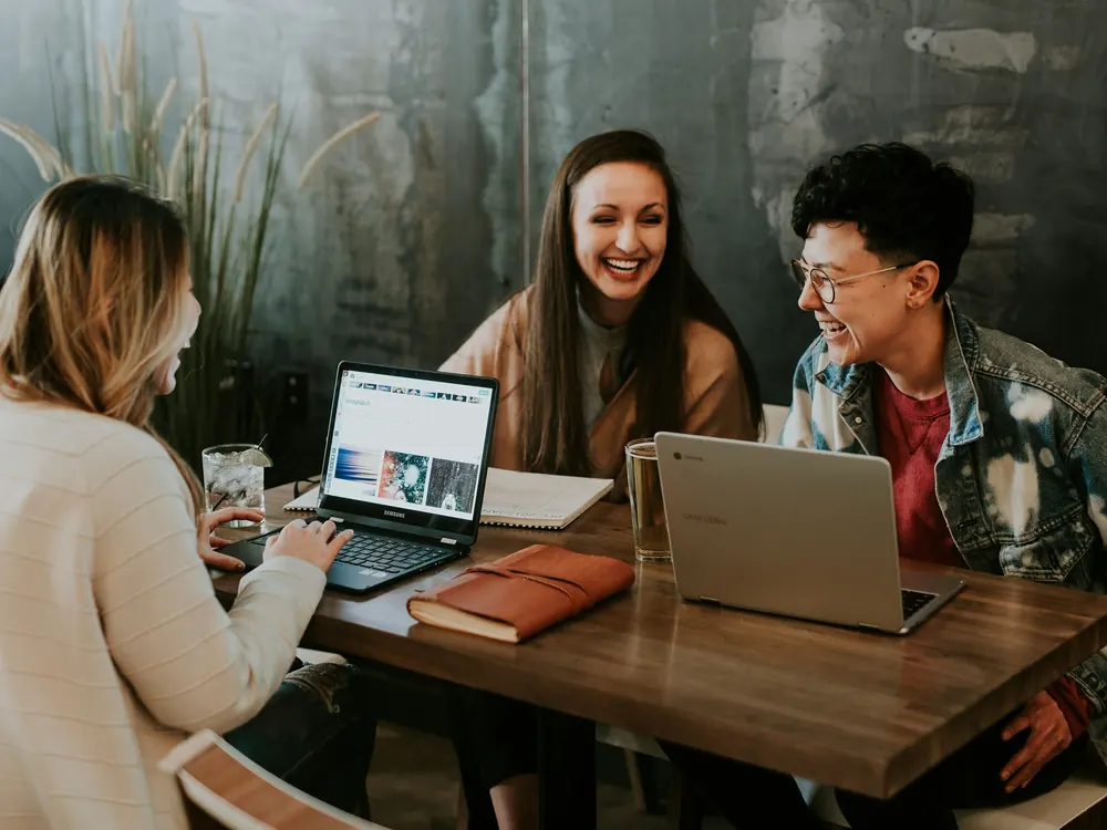 Three professionals collaborating around laptops in a shared workspace